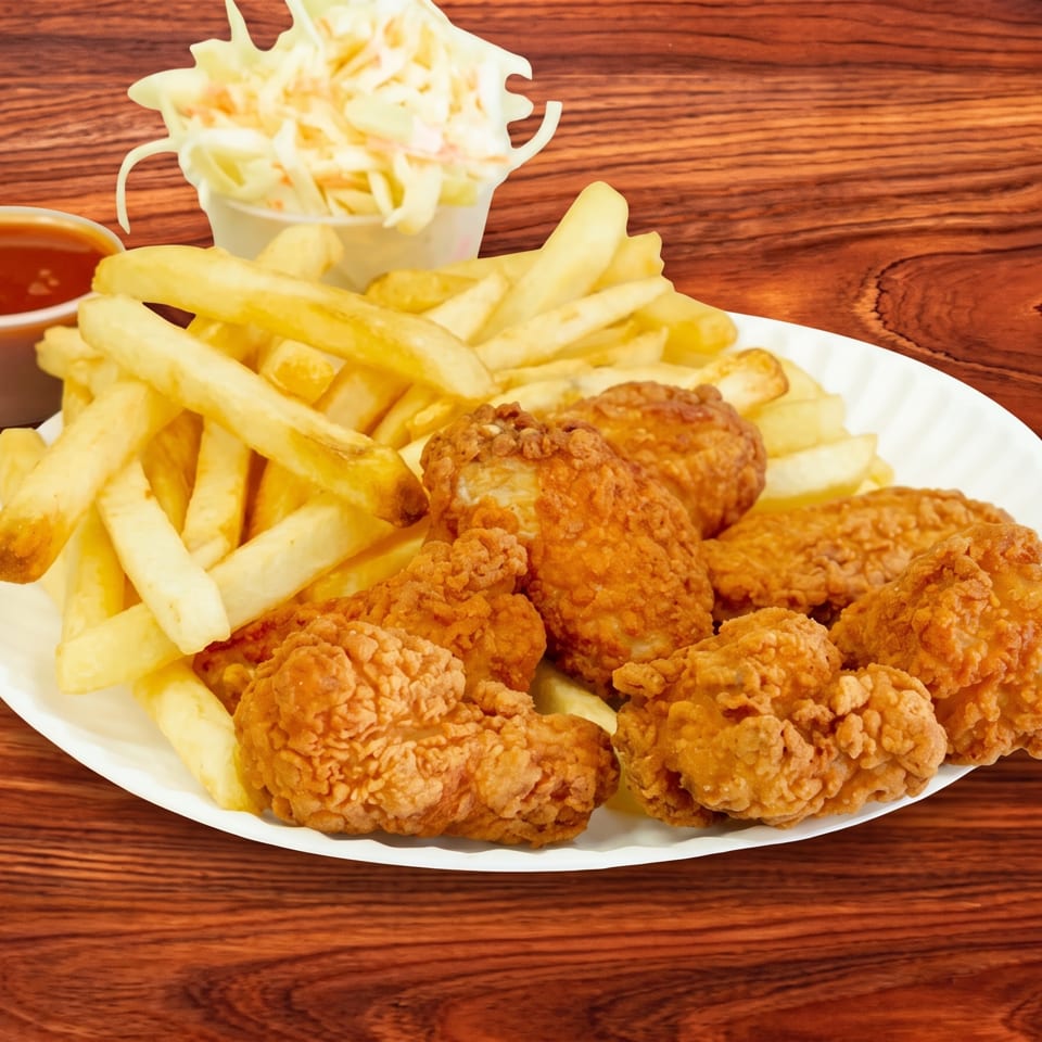 Crispy fried chicken pieces, golden french fries, coleslaw, and dipping sauce on a wooden table.