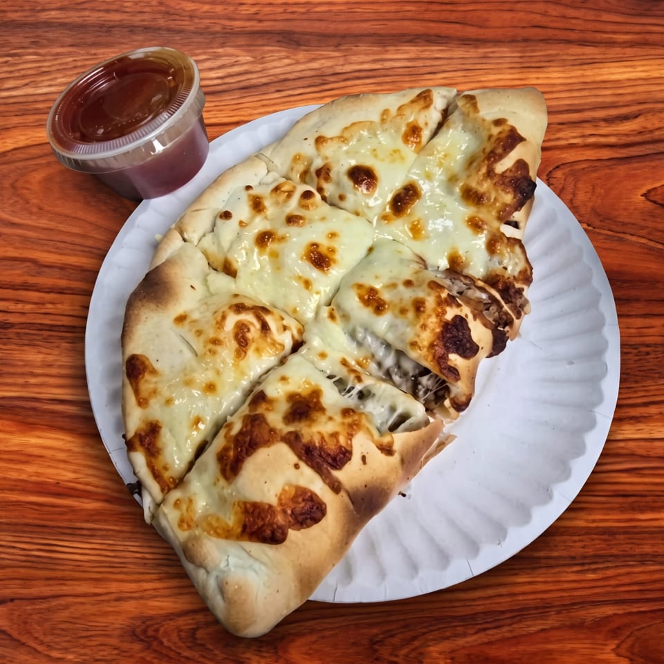 Cheesy calzone slices on a white paper plate with a side of dipping sauce on a wooden table.